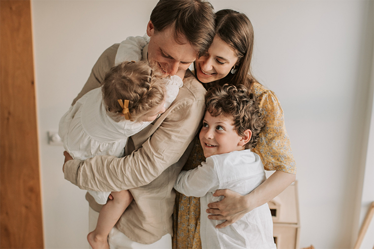 Family of four hugging, with little girl being lifted up by father and older brother hugging mother